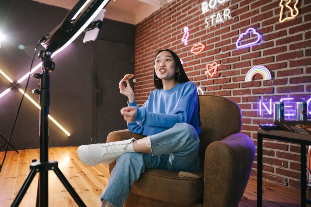 pexels photo 7676402 7676402 Young Asian woman streaming live indoors with neon lights, engaging audience through technology and creative content.